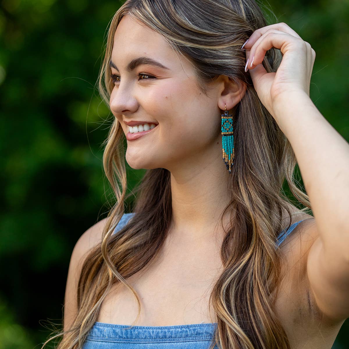 Woman with long hair and blue earrings against a blurred green background