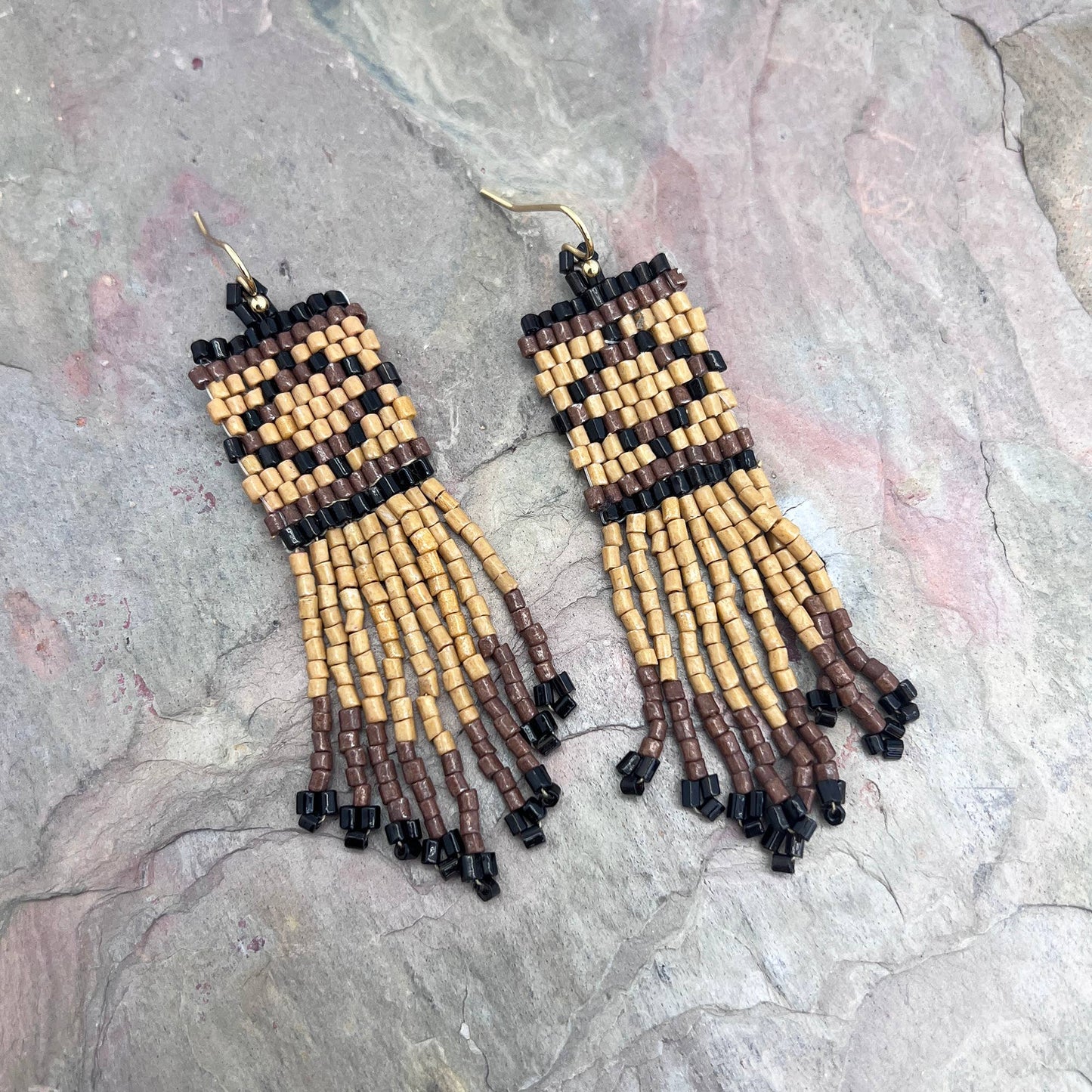 Beaded earrings with brown, beige, and black beads on a stone surface