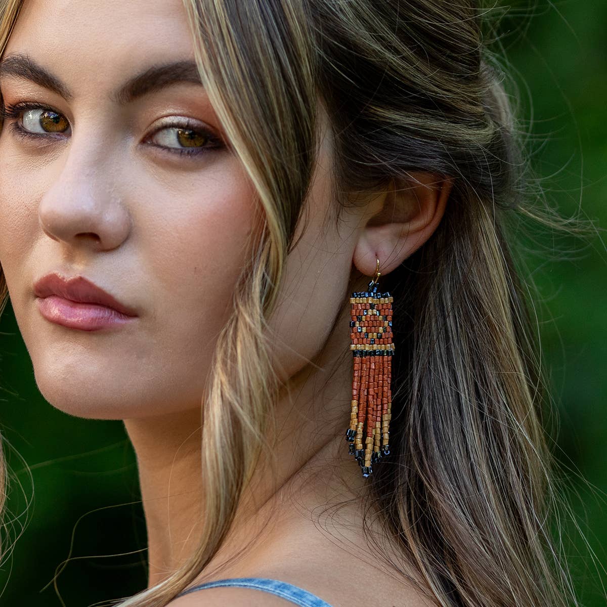 Close-up of a woman wearing colorful beaded earrings with a blurred green background