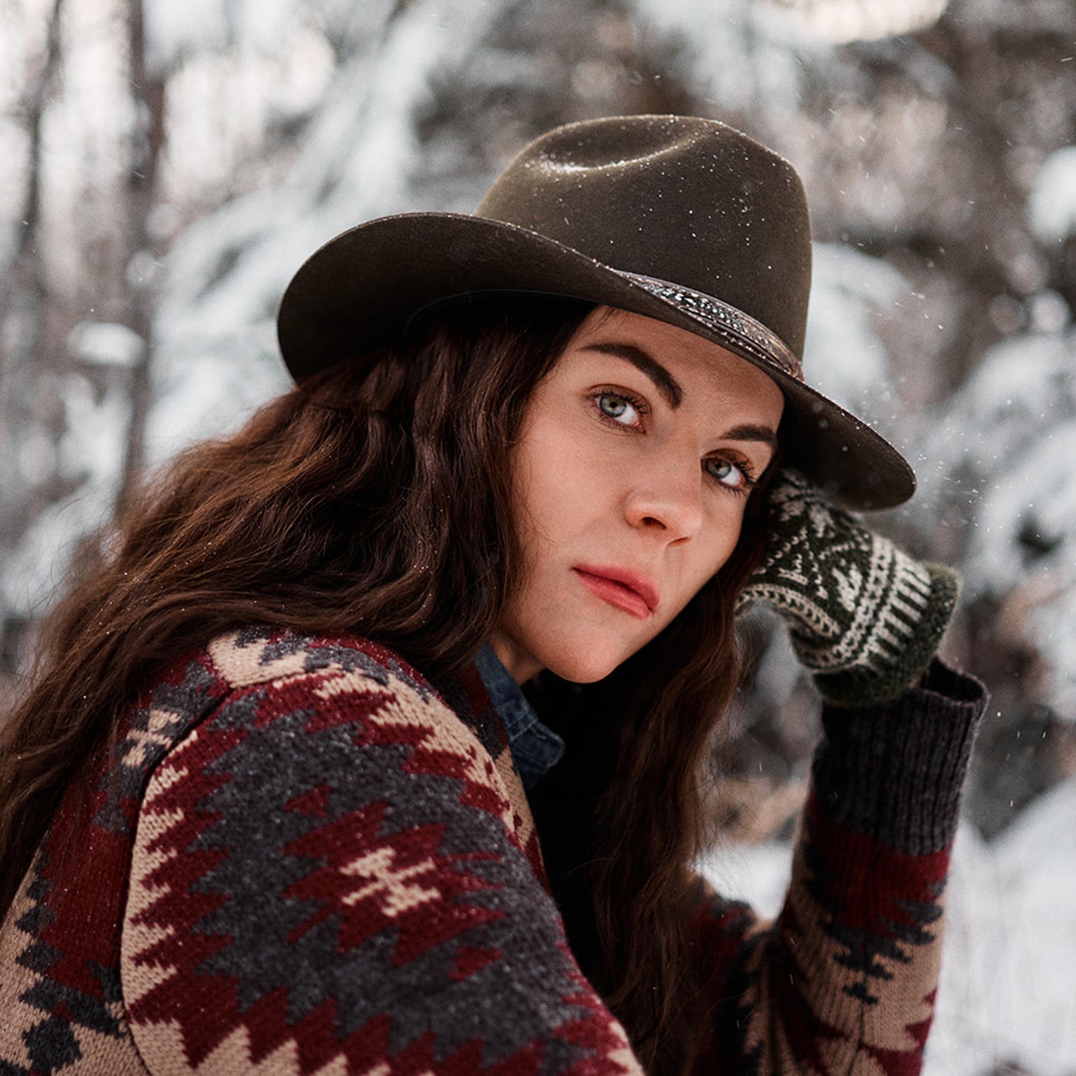 Woman in a snowy forest wearing a Stetson hat and sweater