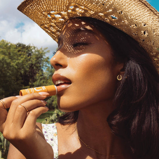 Woman applying lip balm outdoors with a straw hat
